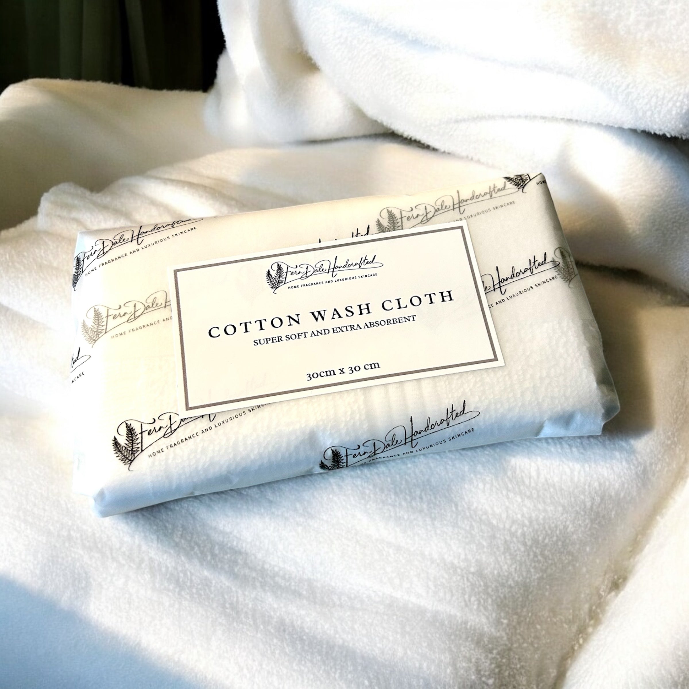 Cotton Wash Cloth wrapped in branded paper with a rectangular label, resting on white textured fabric.
