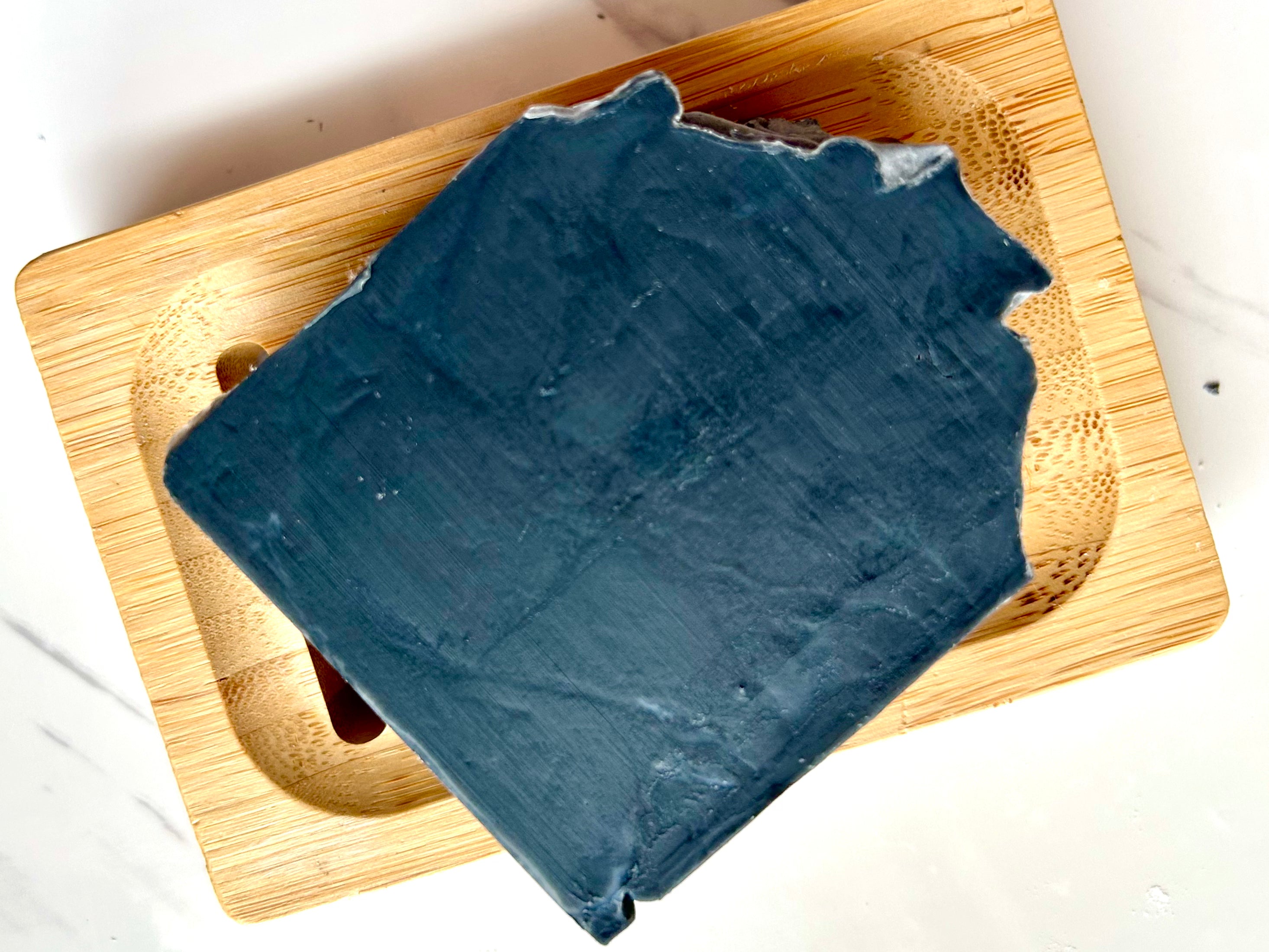 Smoke & Stillness - Tea Tree (Shadow) Tallow Soap, a dark blue bar with uneven edges on a wooden soap dish.